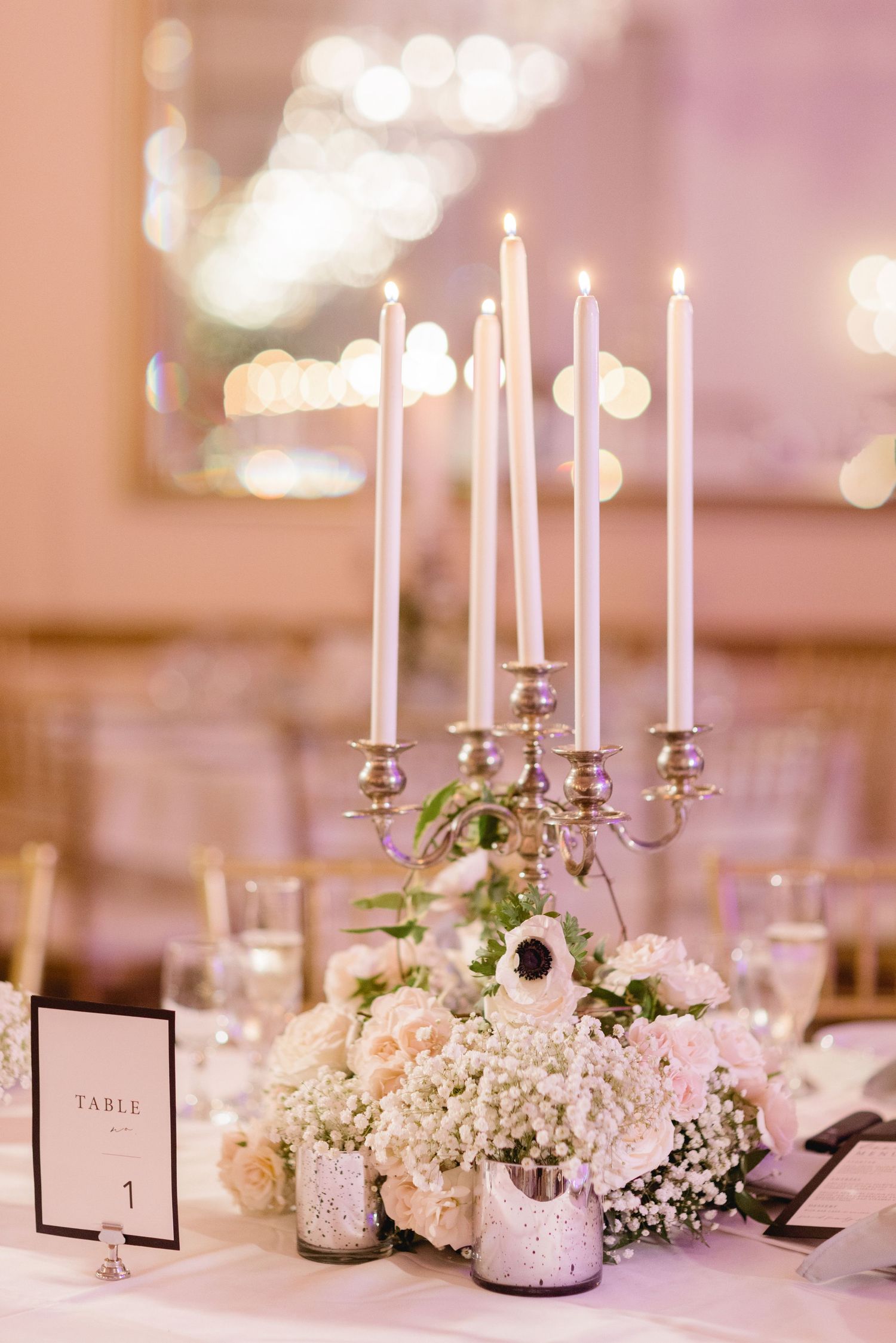 Romantic table centerpiece with white taper candles and delicate floral arrangements.