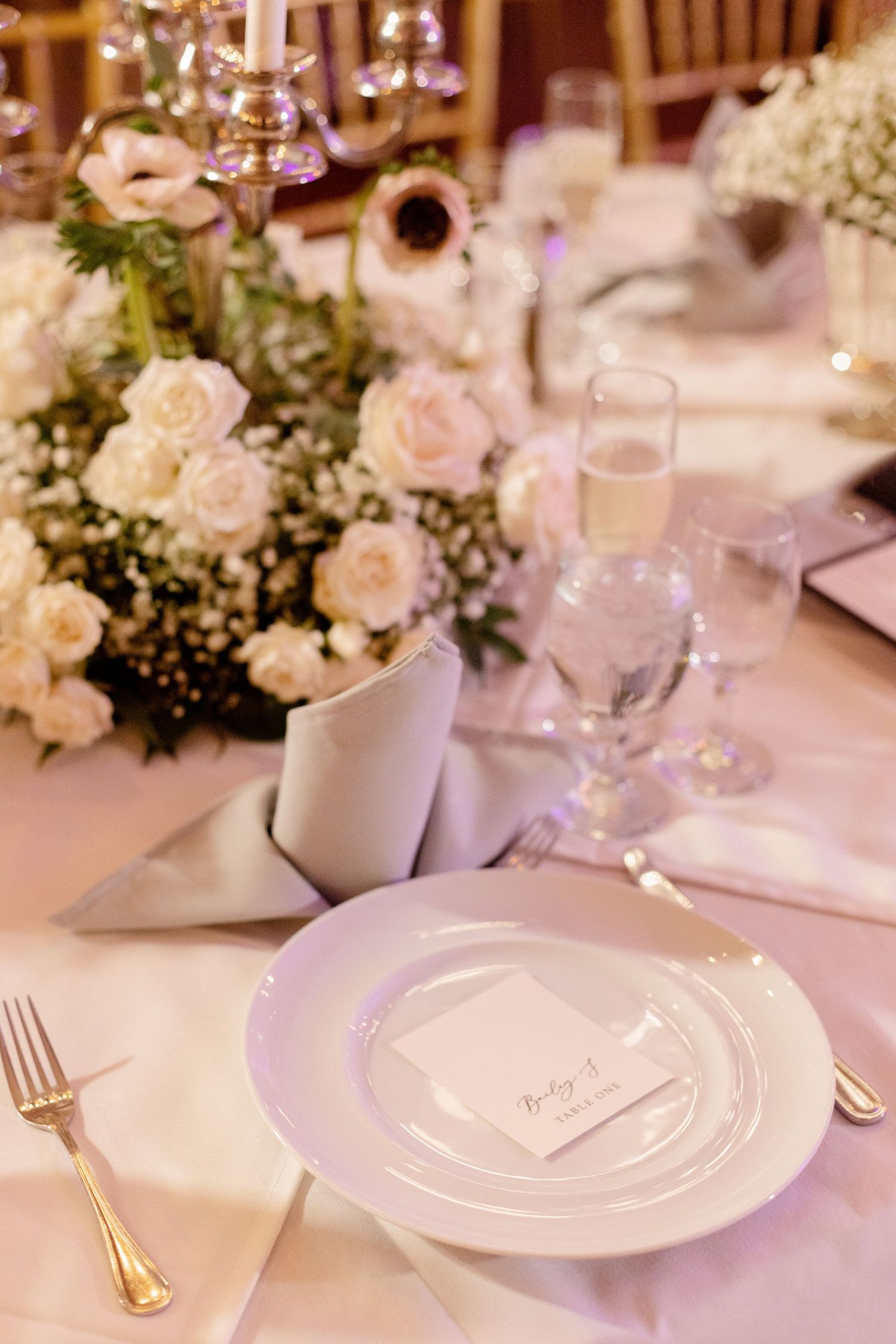 Elegant wedding reception table setting with pink roses, crystal glasses and gold flatware.