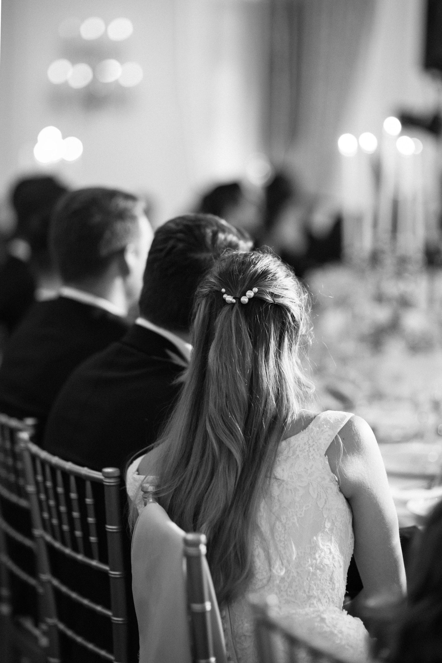 Wedding guest in lace dress seated at reception dinner table with soft bokeh lights.