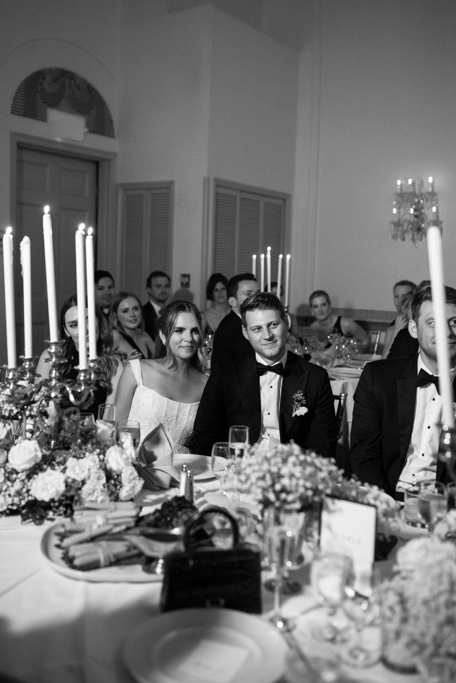Black and white photo of wedding reception dinner with candelabras and formal table settings.