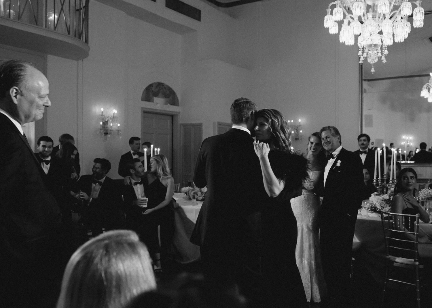 A formal gathering of people in elegant eveningwear at a banquet hall illuminated by crystal chandeliers.