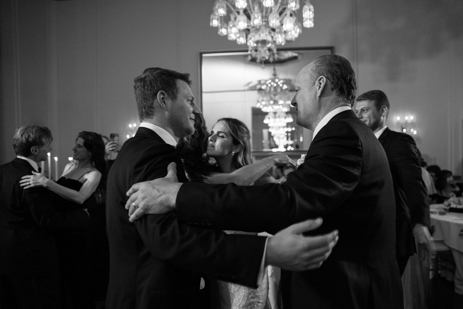Couples dance together at an elegant black and white evening reception under sparkling chandeliers.