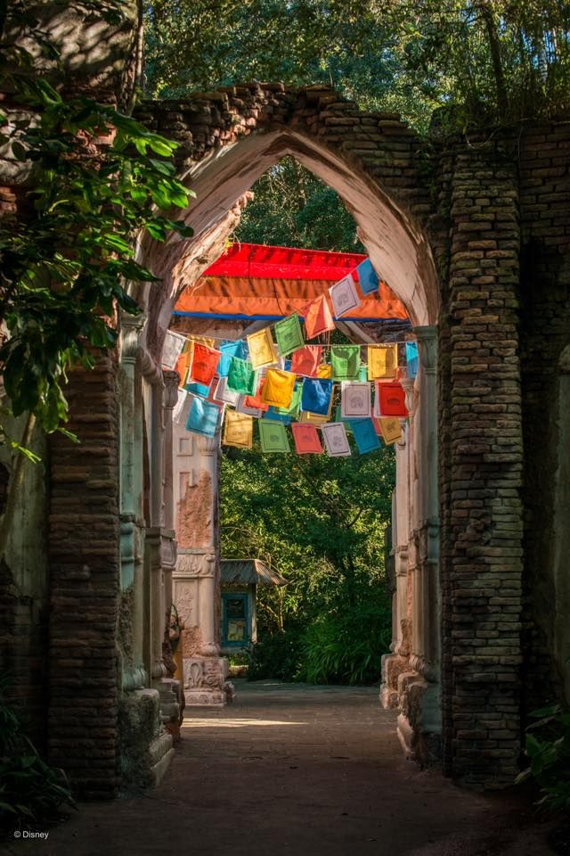 Stone archway decorated with colorful Tibetan prayer flags in a lush garden setting.