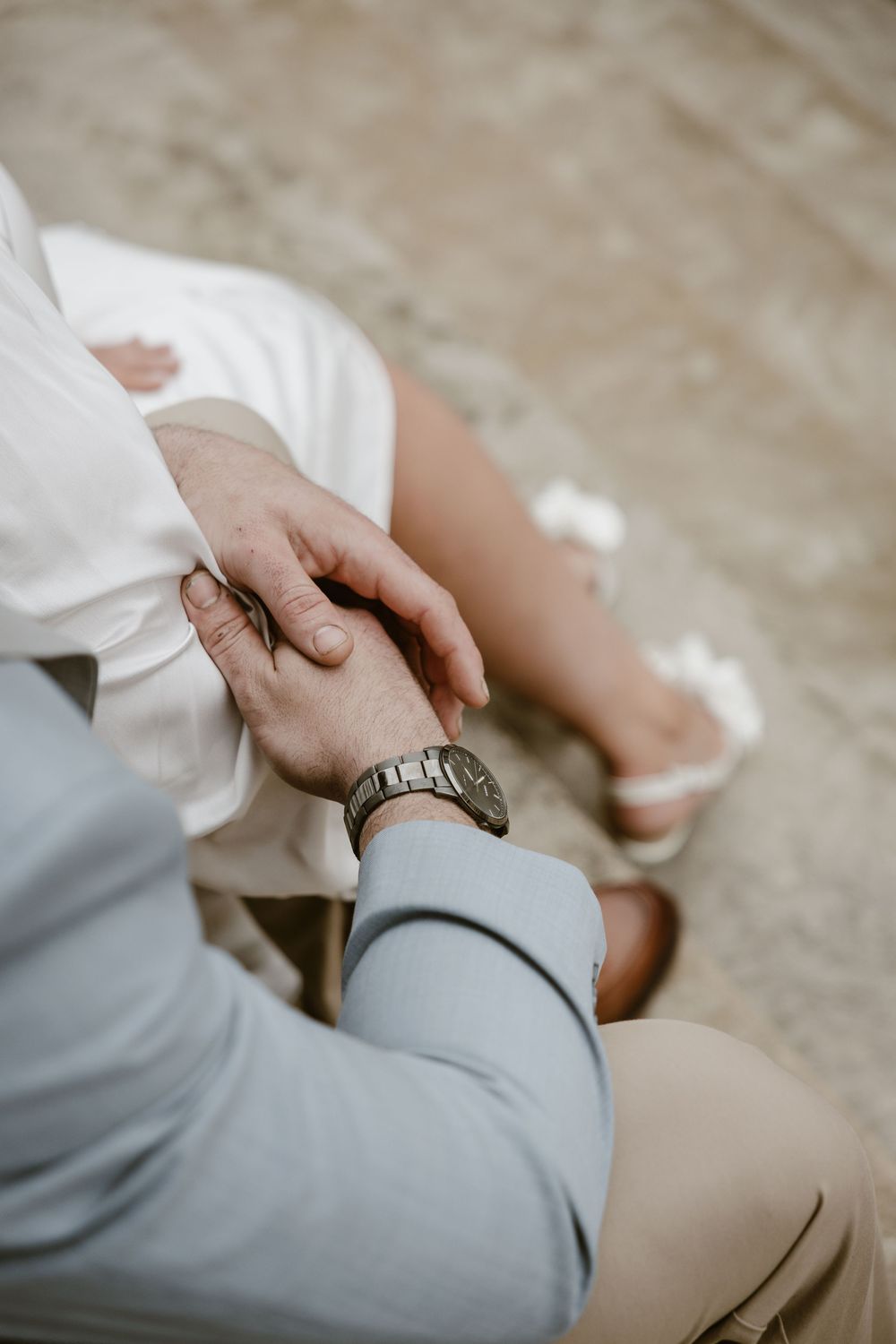 Closeup of couple holding hands showing wedding attire with gray suit sleeve and white dress details.