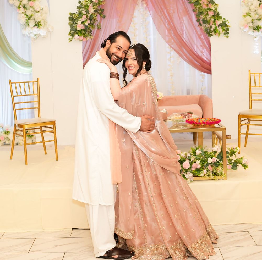 Couple in traditional South Asian attire embracing at an elegant wedding ceremony with pink floral decor.