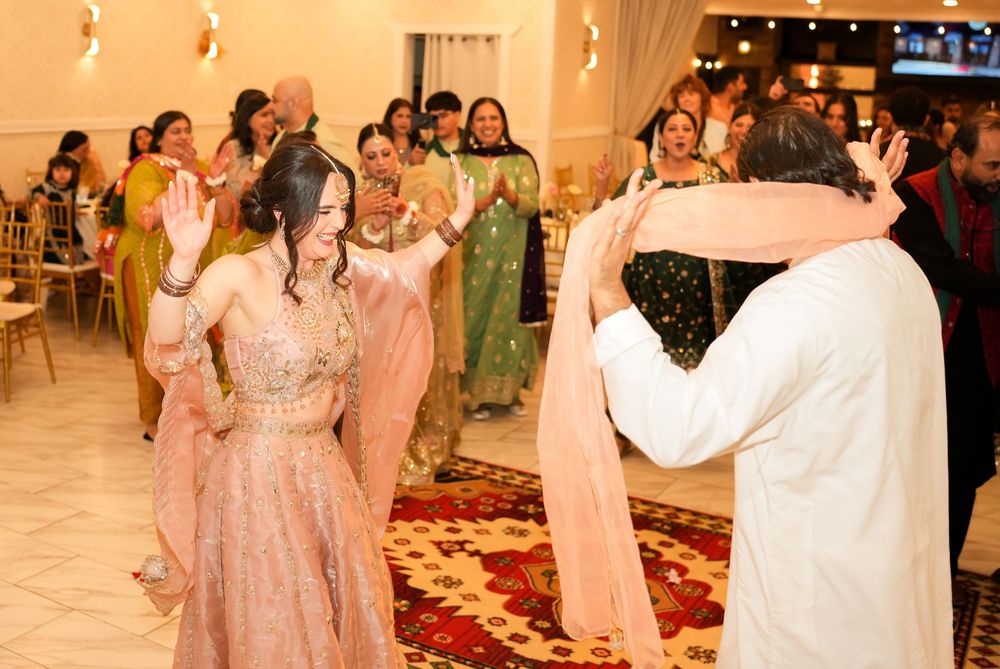 Couple dancing at South Asian wedding celebration with guests clapping in elegant decorated venue.