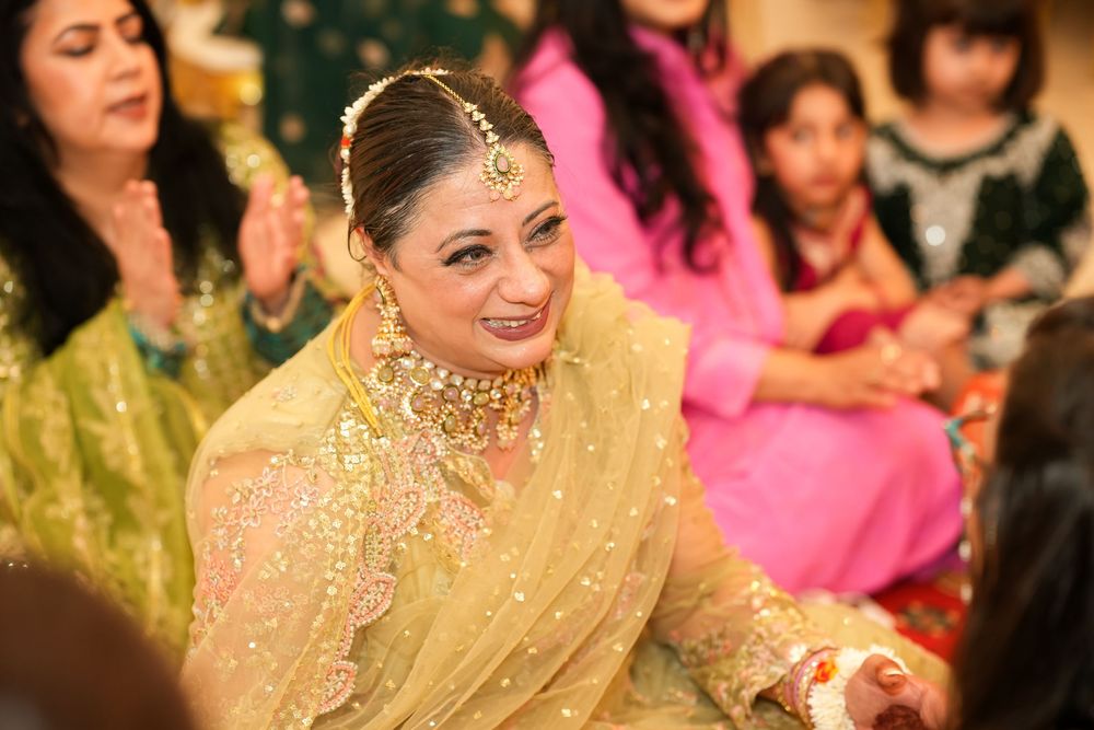 A bride in gold embroidered attire and jewelry smiles during a South Asian wedding ceremony.
