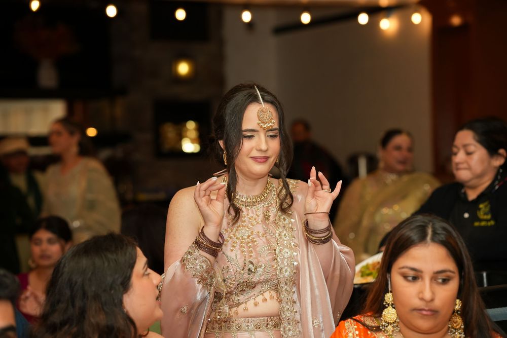 Woman in elegant Indian bridal lehenga with gold embroidery dancing at a traditional celebration event.