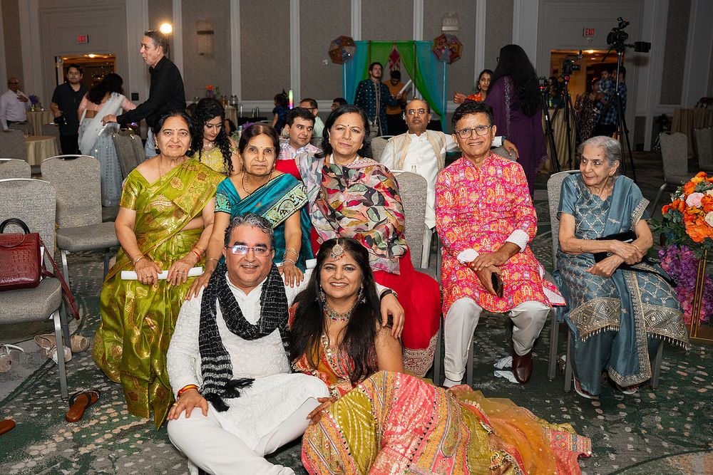 Indian family group photo at a festive celebration, wearing colorful traditional attire including sarees and kurtas.