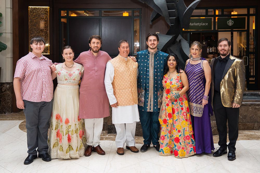 Group of eight people in festive Indian and Western attire posing together at an elegant indoor venue.