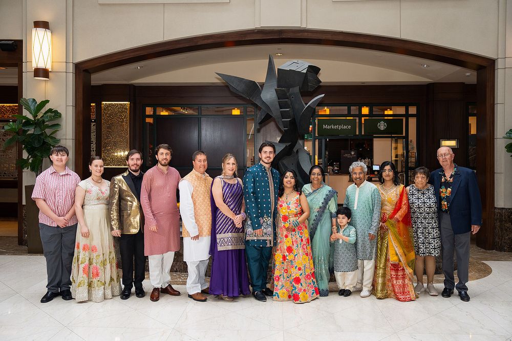Large Indian family group posing in traditional colorful attire at an elegant hotel lobby during a wedding celebration.