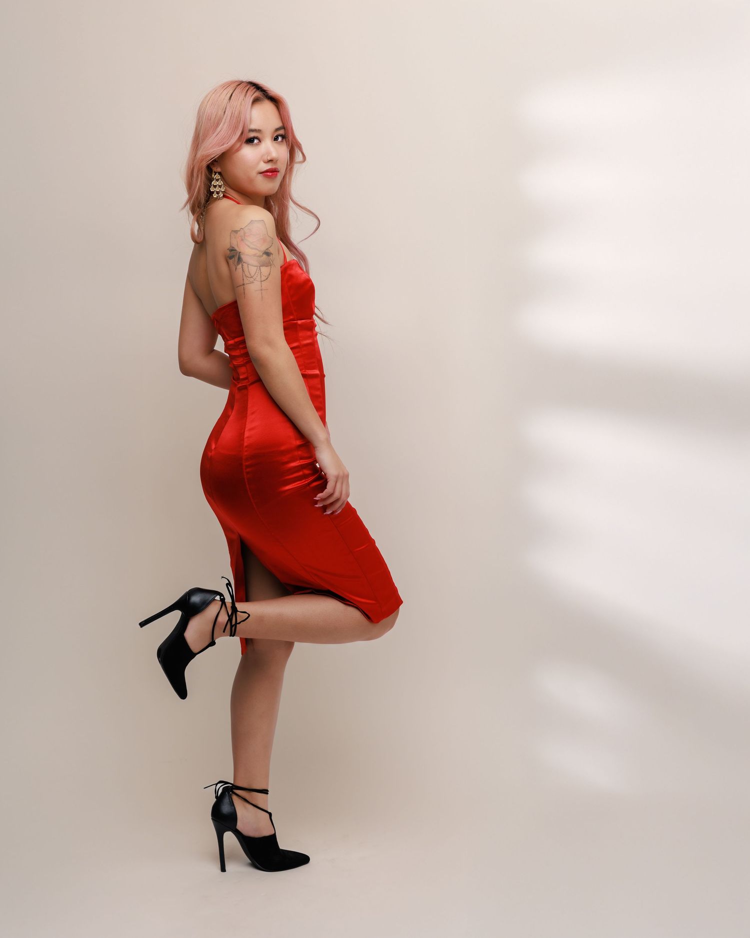 Glamorous pose in fitted red dress and black heels against light studio backdrop.