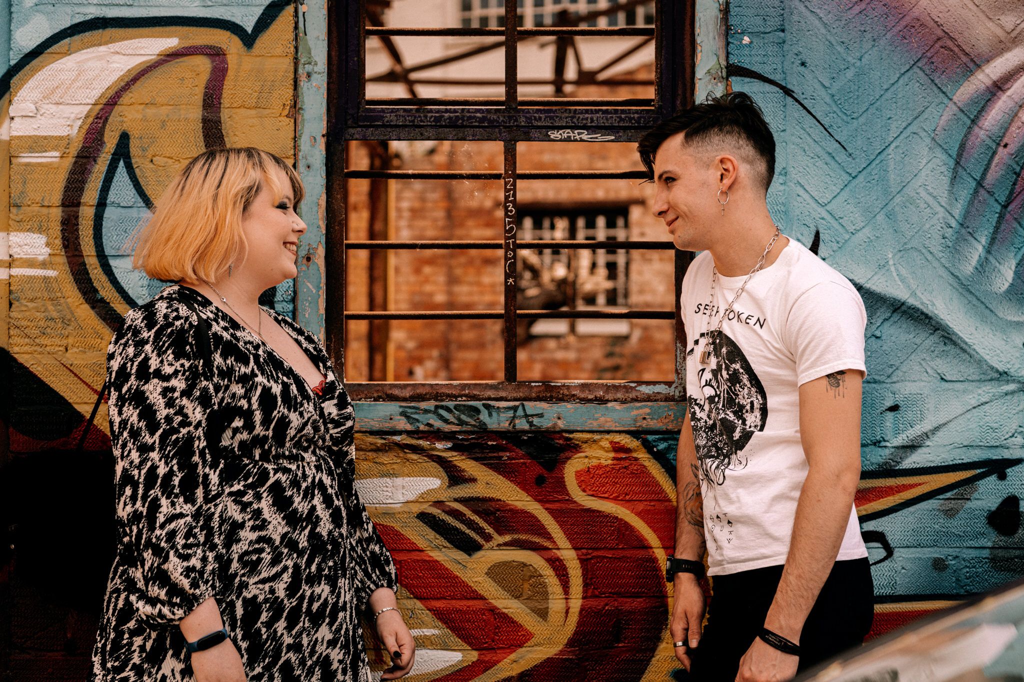 Two people having an animated conversation in front of a colorful graffiti wall at an urban location.