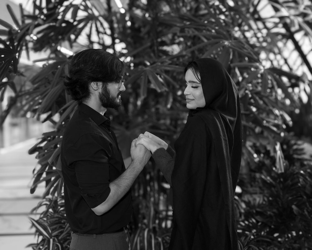 Black and white portrait of a couple holding hands in a garden with tropical foliage in the background.