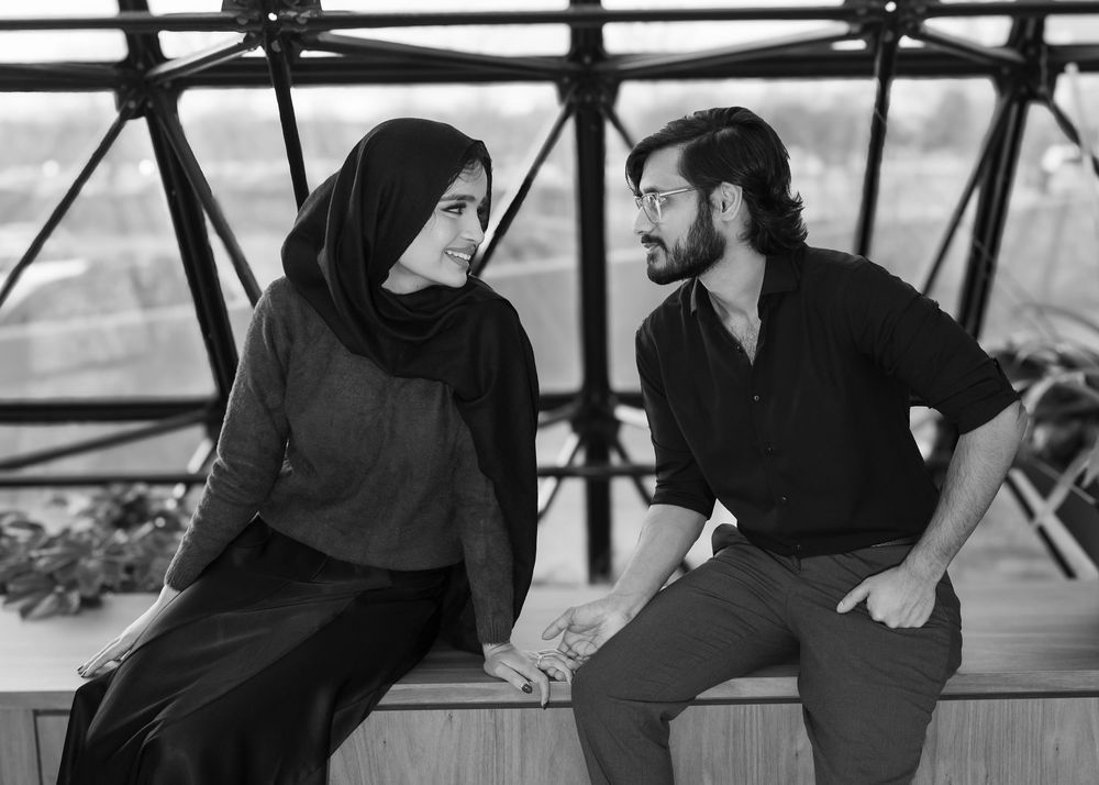 A couple in dark clothing having an intimate conversation while sitting on a wooden deck in black and white.