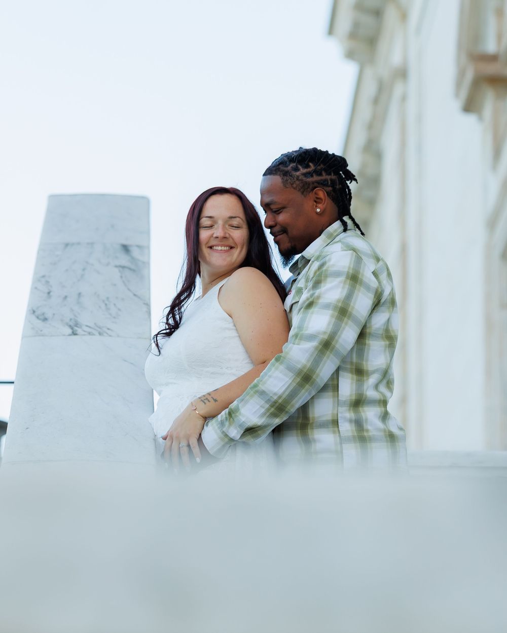 A couple share an intimate embrace against a white marble column background.