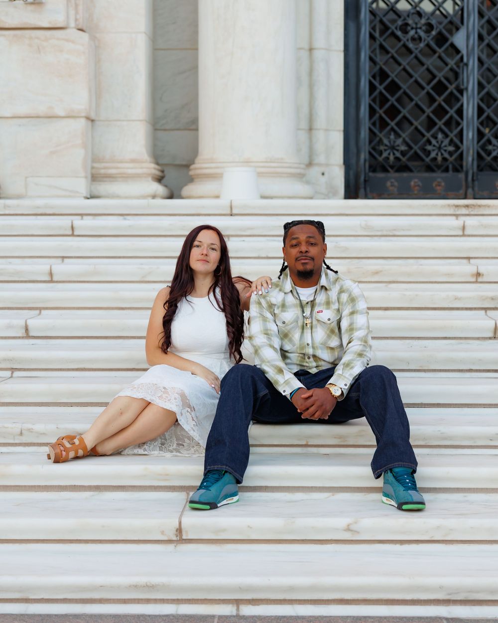 A couple sits together on white marble steps outside a building with classical columns.