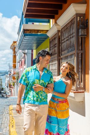 A joyful couple in colorful tropical outfits walks arm-in-arm along a bright cobblestone street in Old San Juan.