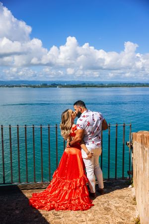 Couple kissing by iron fence with stunning turquoise Caribbean sea backdrop in Puerto Rico.