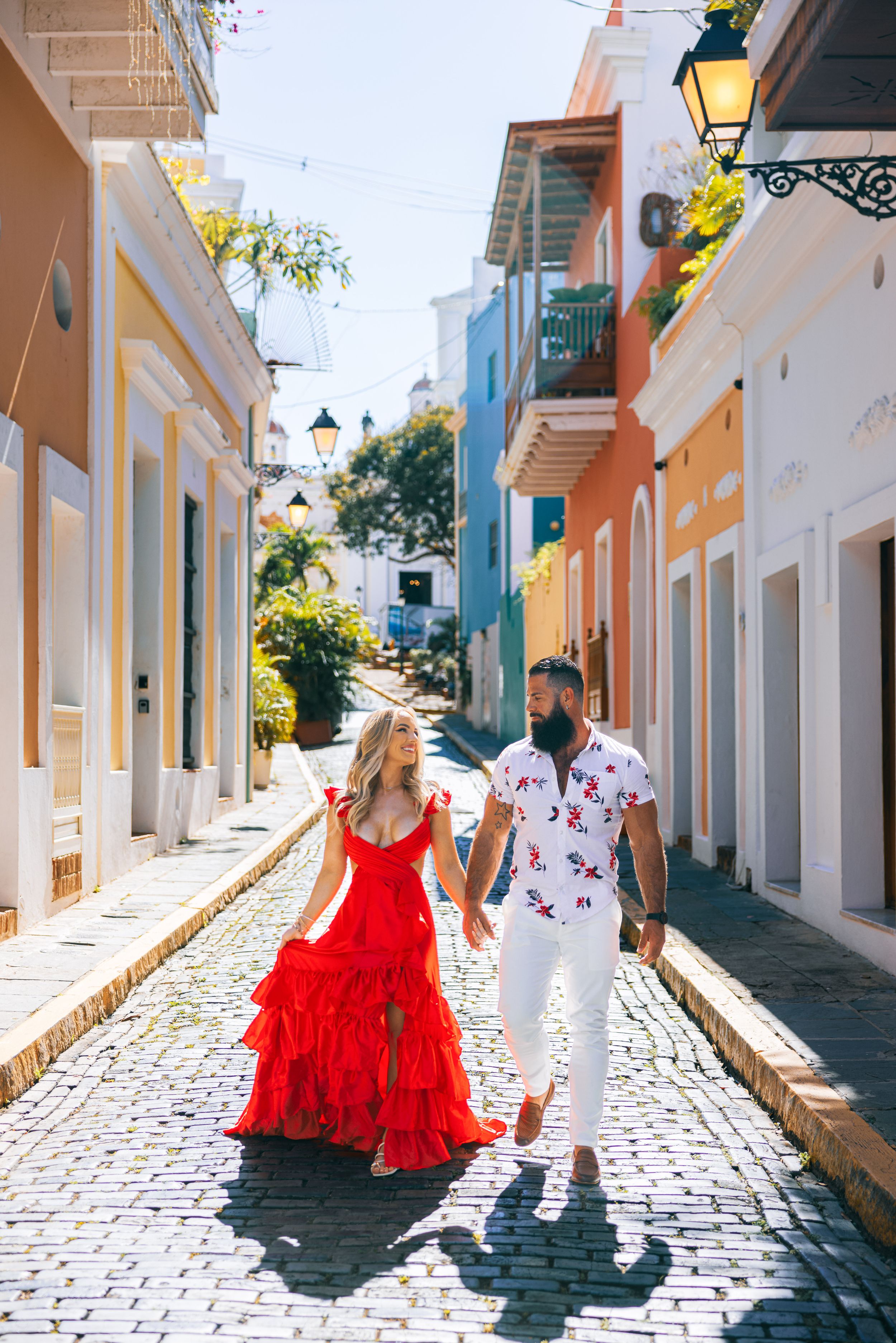Couple in red dress and floral shirt strolling colorful cobblestone street in Old San Juan.
