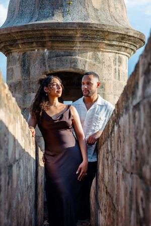 Elegant couple posing in a historic stone fortress sentry box in Old San Juan.