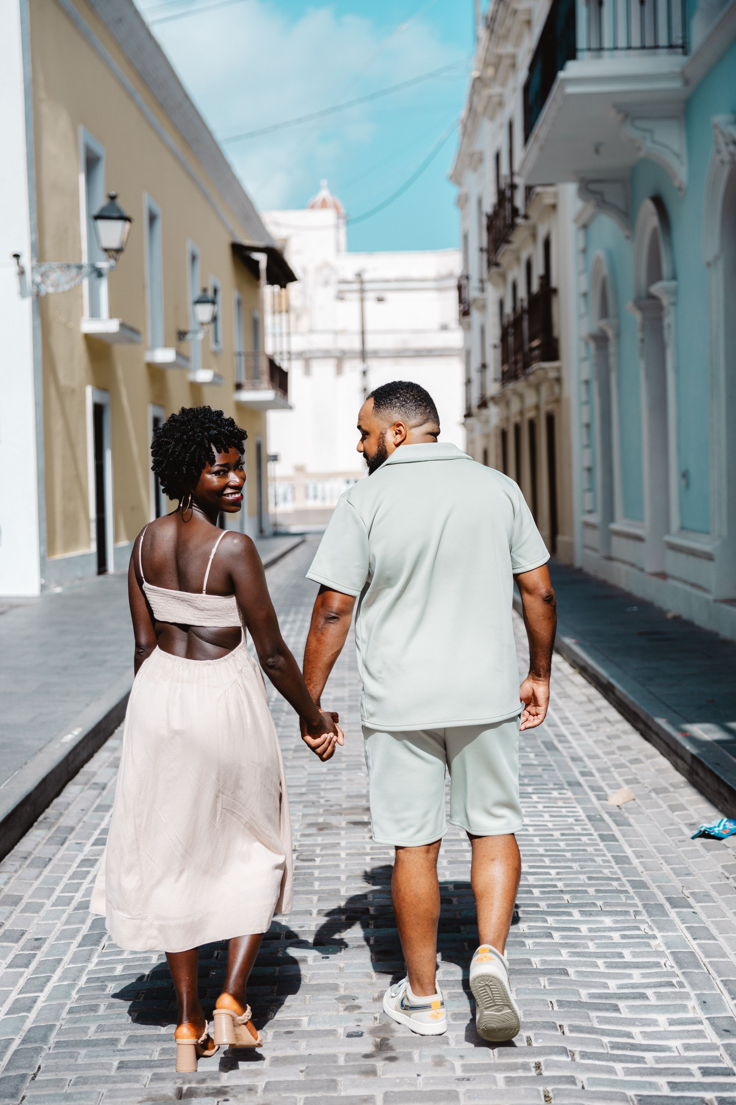 Couple walking hand in hand down sunny cobblestone street in Old San Juan, Puerto Rico.