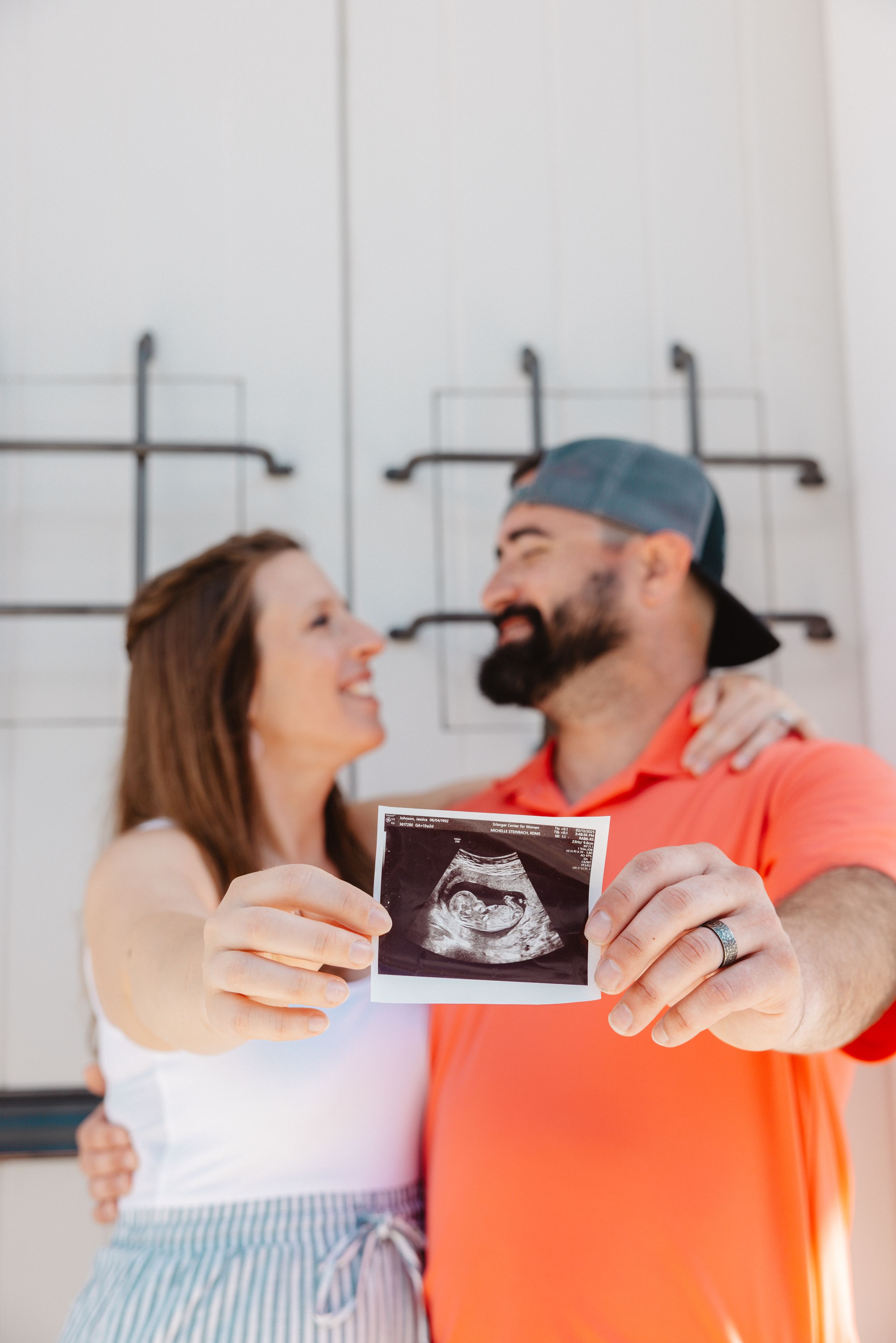 A happy couple holds up an ultrasound photo together, smiling at each other in a pregnancy announcement.