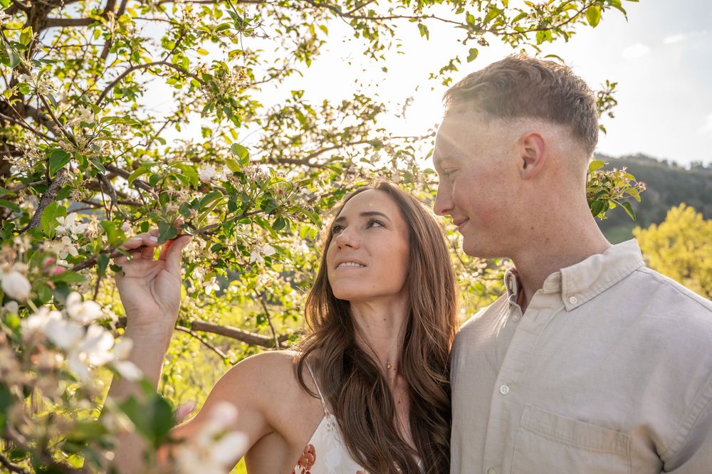 Couple enjoying a romantic moment among blooming tree branches in warm golden sunlight during sunset.