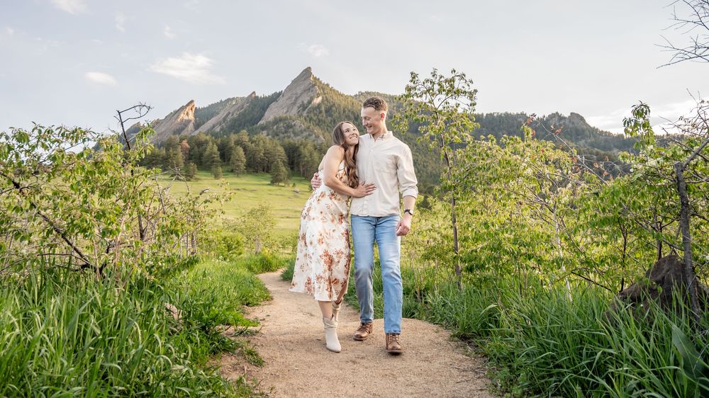 A couple walks hand in hand along a scenic trail with the Flatiron Mountains of Boulder, Colorado in the background.