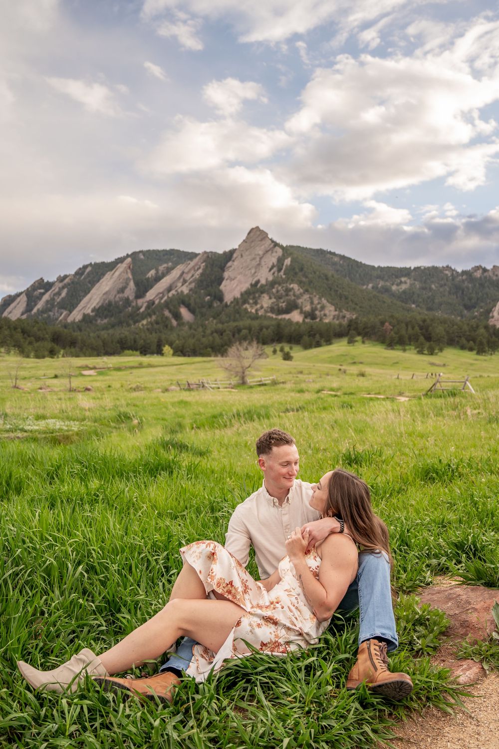 Couple relaxes in green meadow with iconic Flatiron Mountains of Boulder, Colorado as dramatic backdrop.