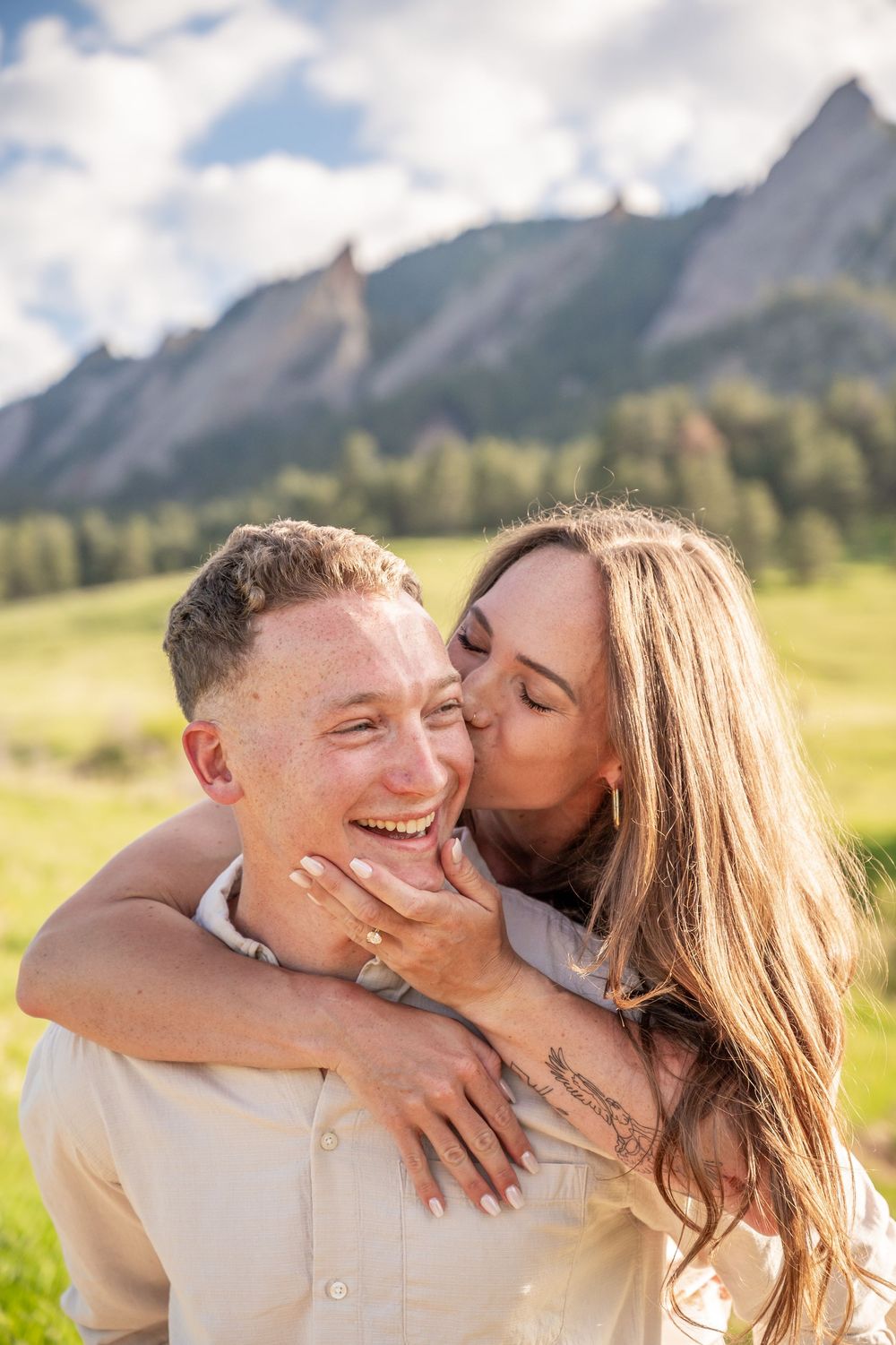 A couple shares a joyful moment together in a mountain meadow with the Flatirons rock formation visible in the background.