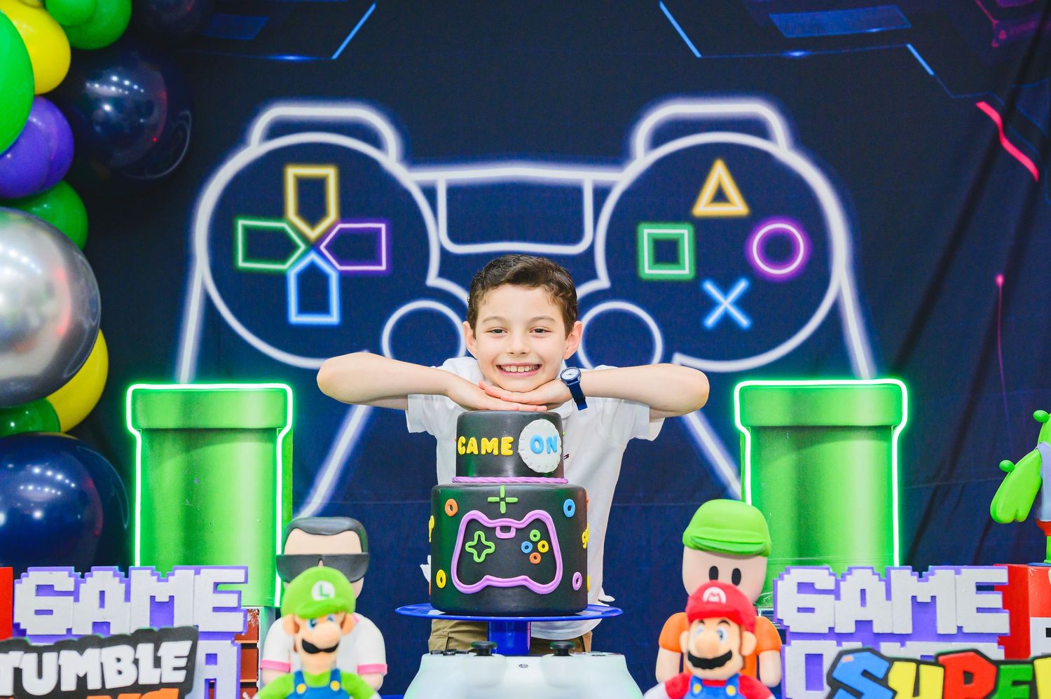 Gaming themed party backdrop with neon controller light, green pipes, colorful balloons and video game character decorations.