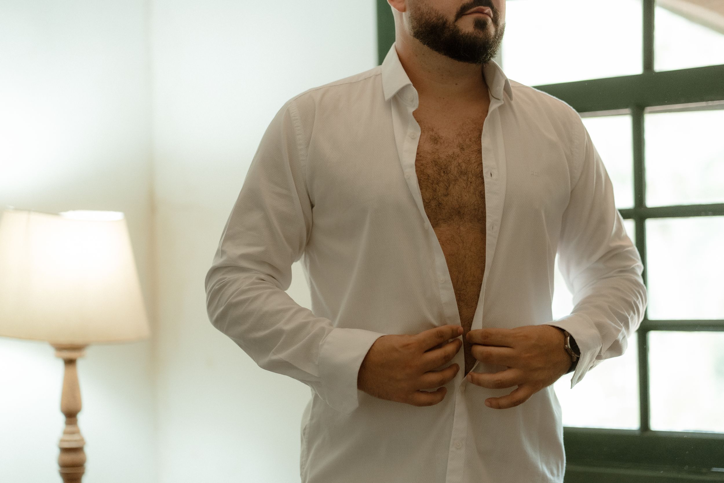 Man wearing a white dress shirt in an elegantly lit room getting ready.