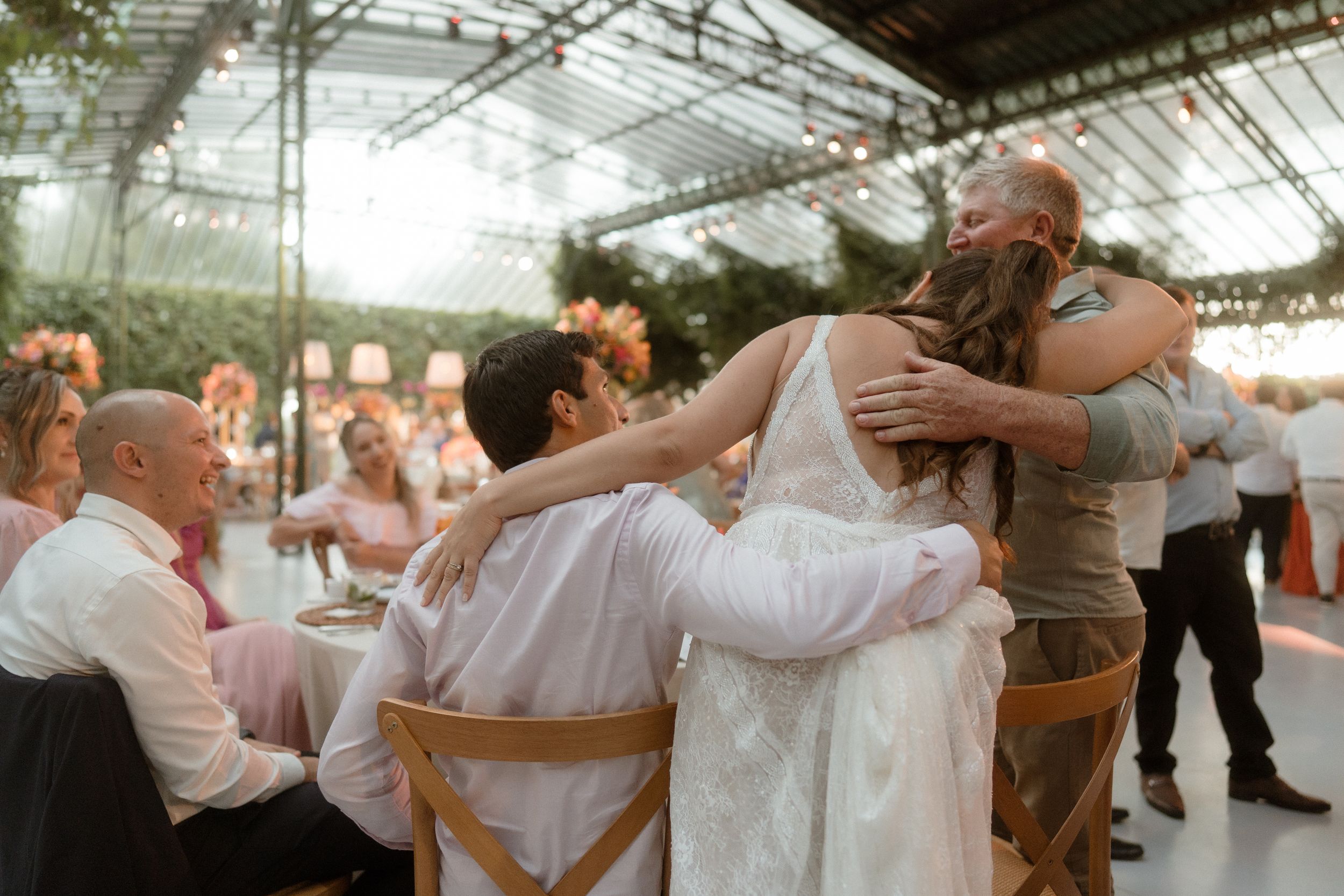 Wedding guests dance in a circle with arms around each other during reception celebrations.