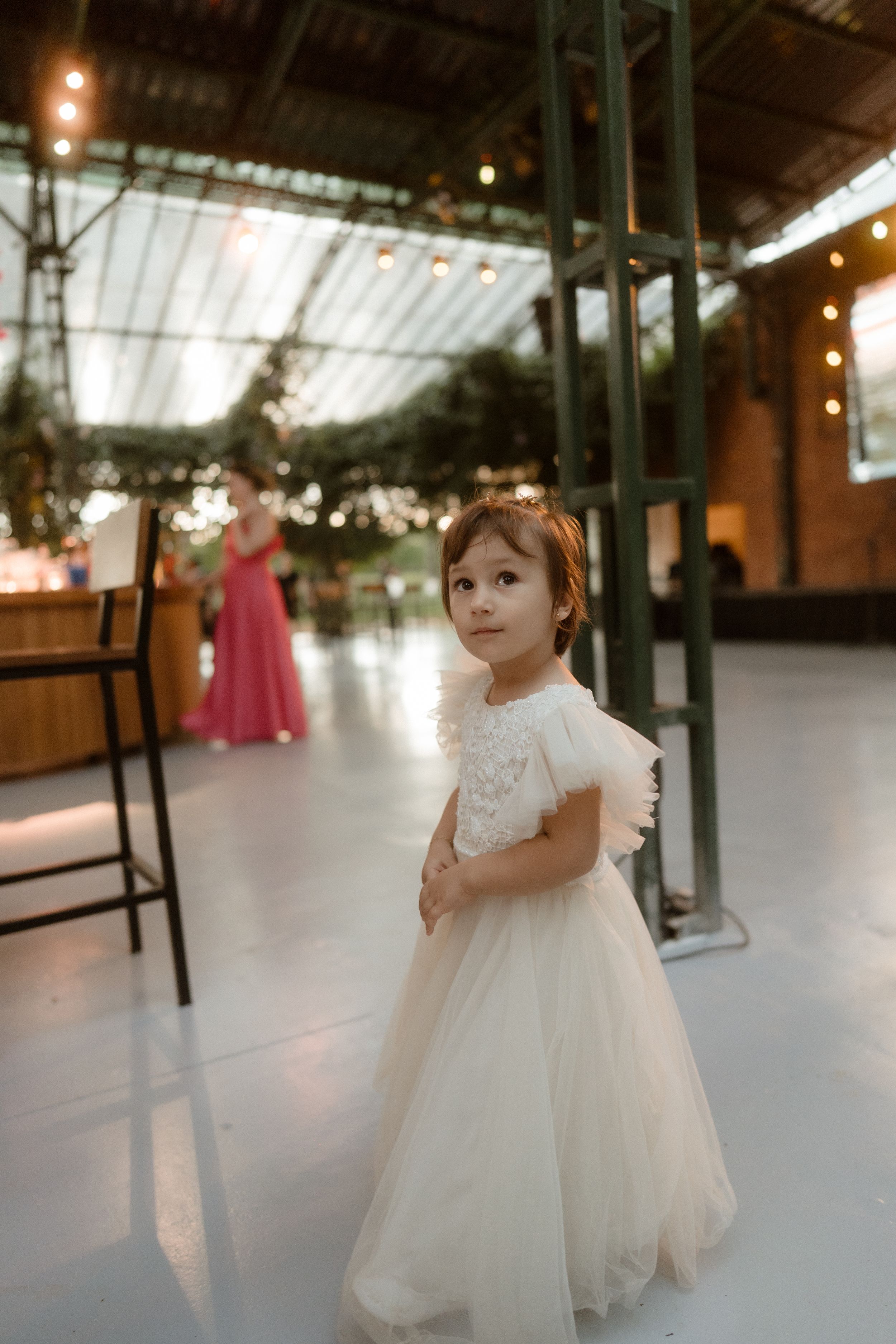 Young flower girl in white dress twirls on dance floor at wedding reception.