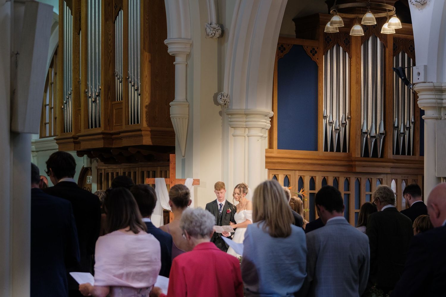A congregation gathers in a church with ornate organ pipes and white arched architecture during a service.
