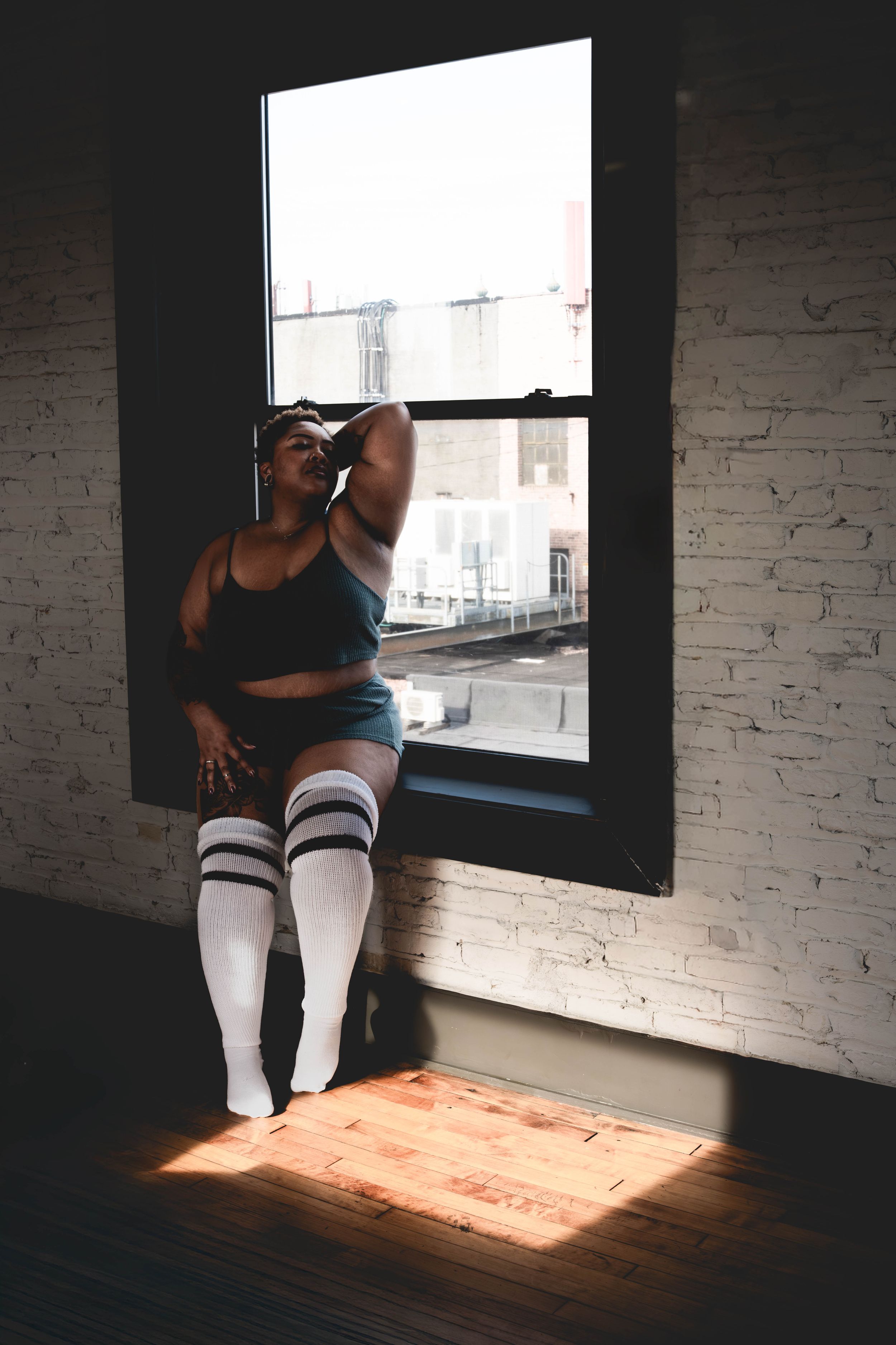 Woman in athletic wear and knee-high socks sits on a sunlit windowsill in a loft space.