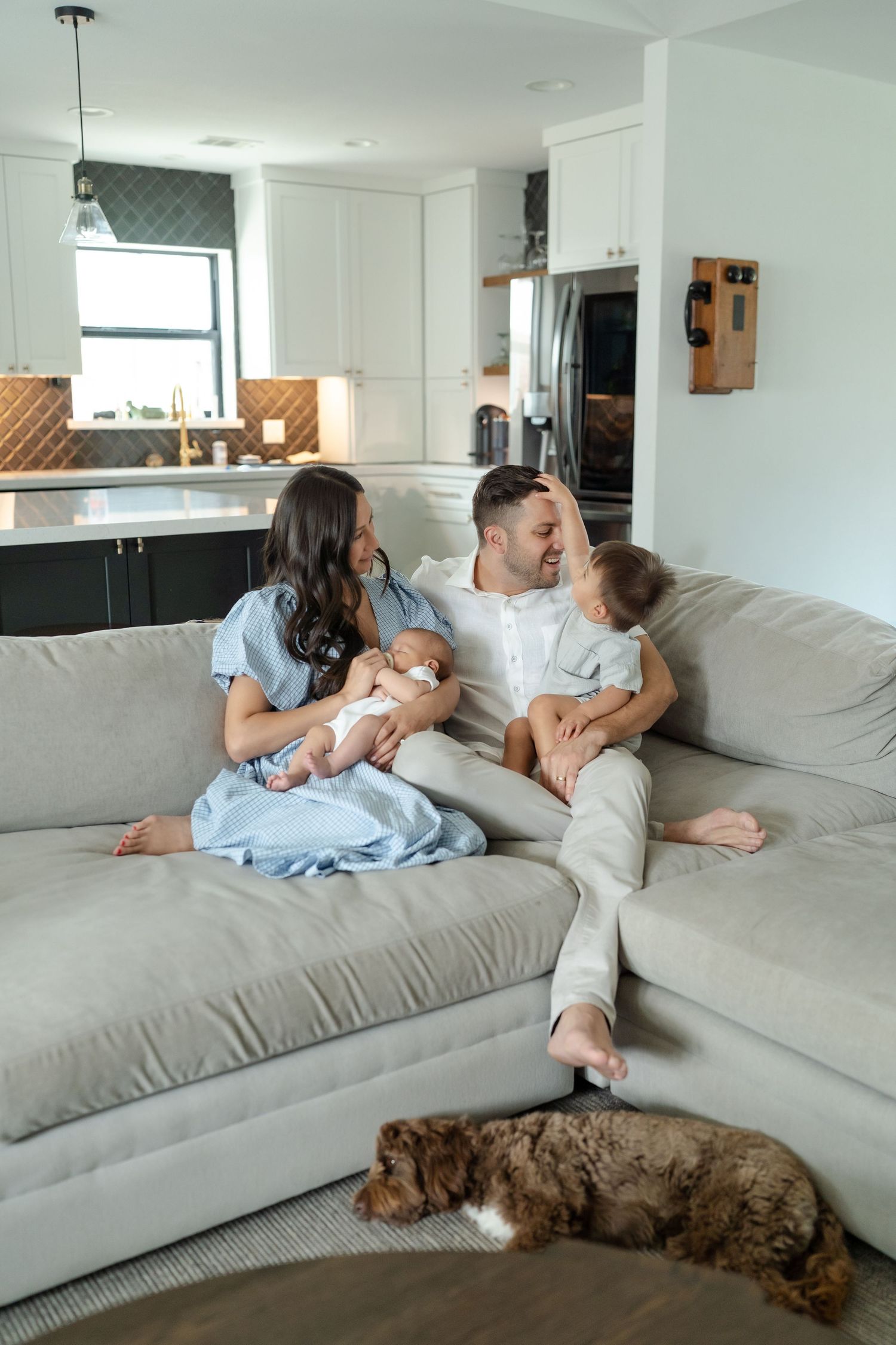 newborn family wearing neutral tones photo in living room on the couch, mom wearing baby blue dress