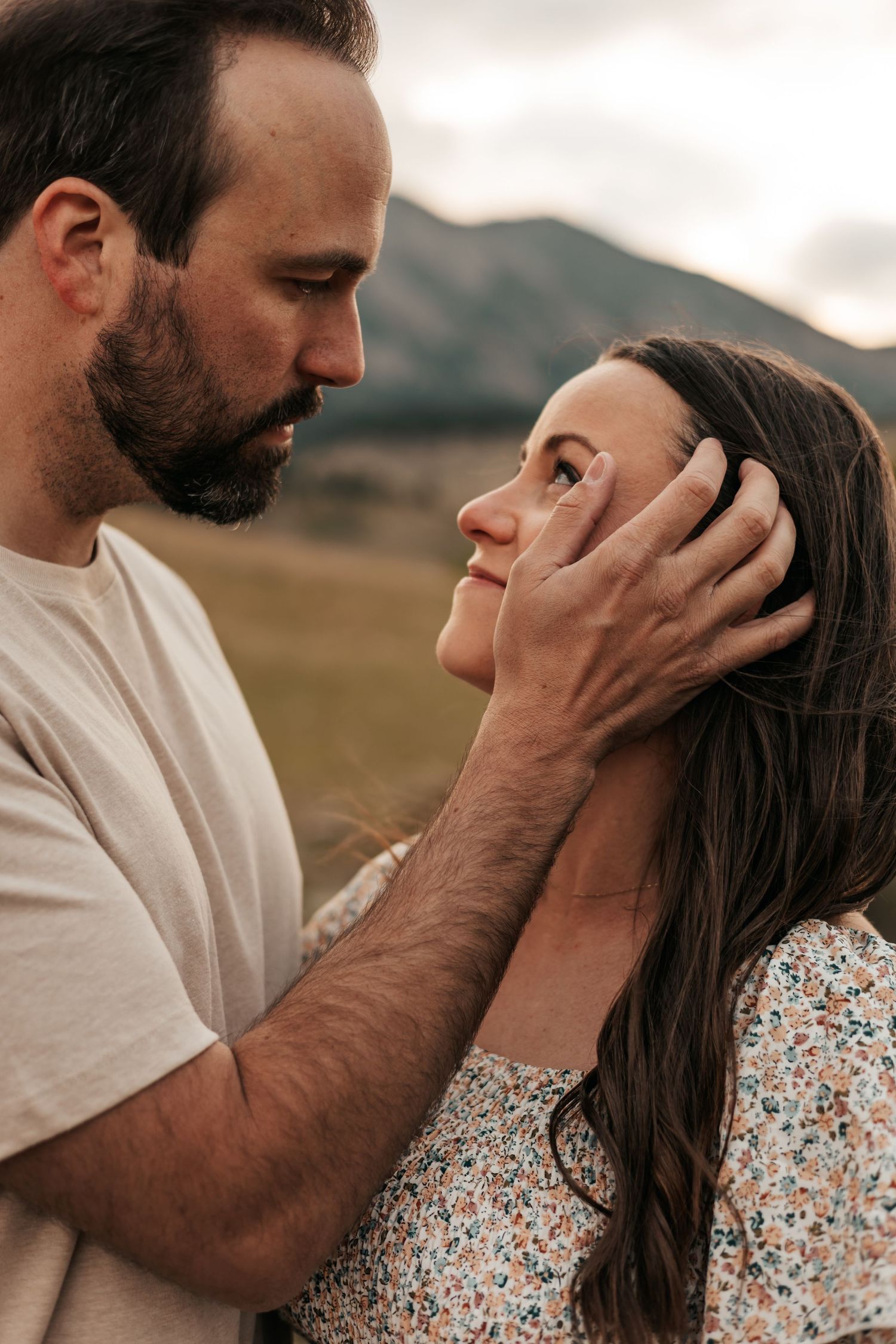 Pregnant woman in floral dress cradling baby bump on rural dirt path with rolling hills backdrop.