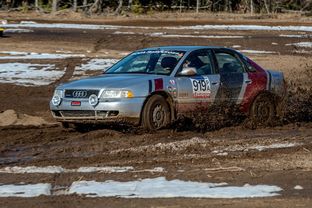 Silver Audi rally car number 913 racing through muddy terrain during an off-road competition event.