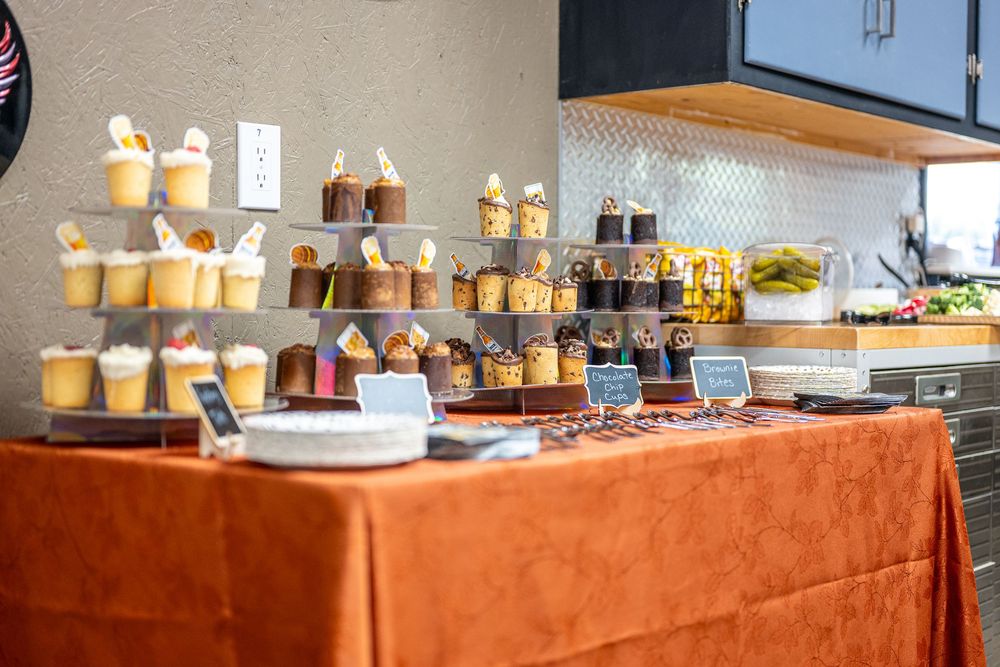 Elegant dessert buffet table with assorted cupcakes, chocolates, and sweet treats displayed on an orange tablecloth.