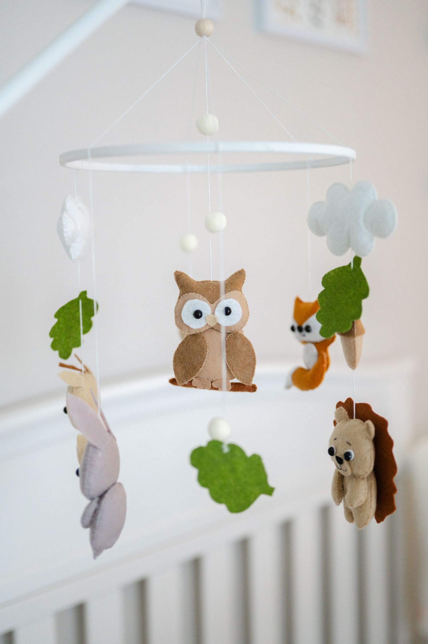 A whimsical woodland nursery mobile featuring felt owl, squirrel, hedgehog, and fox figures with green leaves and white beads.