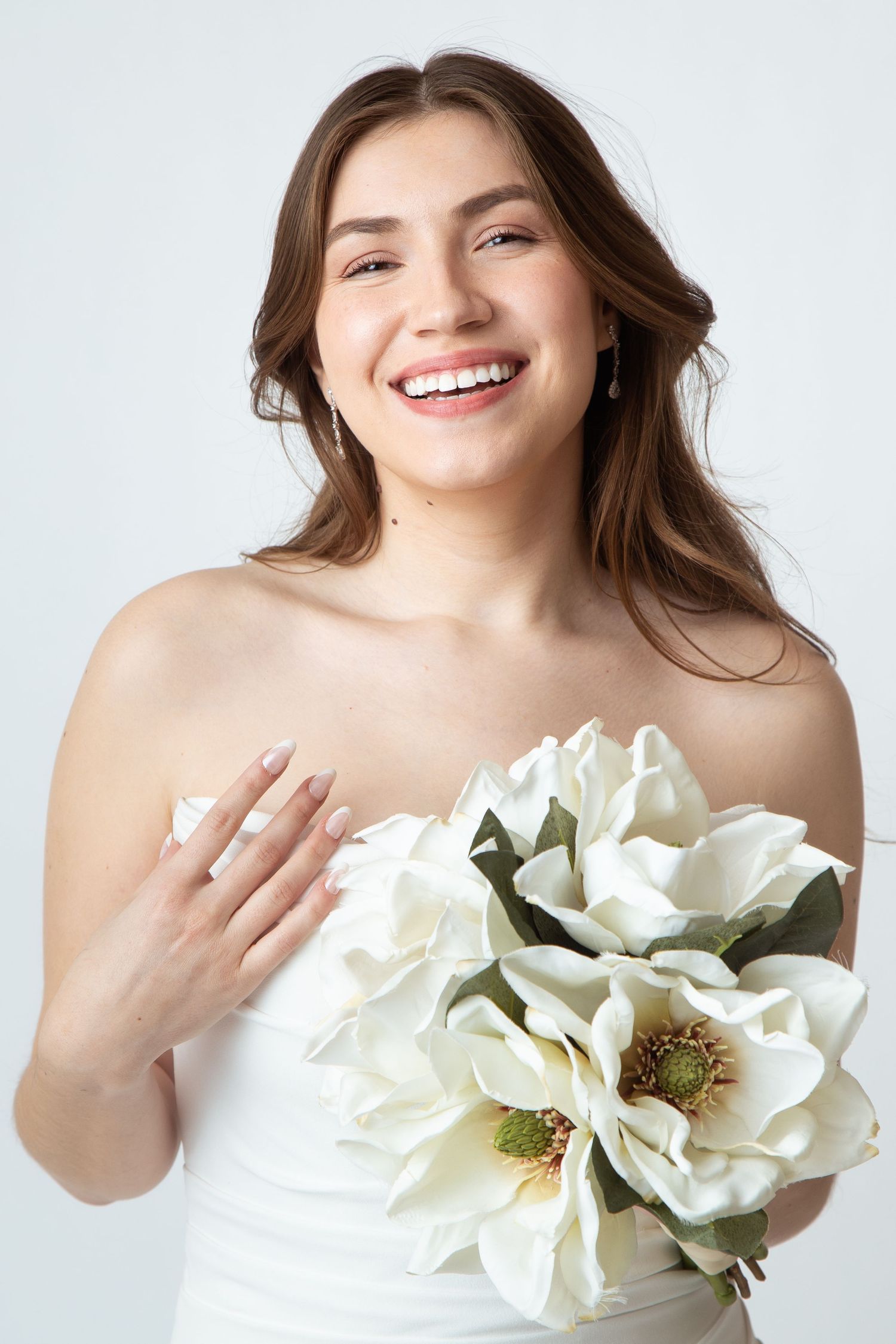 Portrait of a happy bride in a form fitting wedding dress and holding a bouquet of white flowers at Celebrations Bridal and Prom NBTX