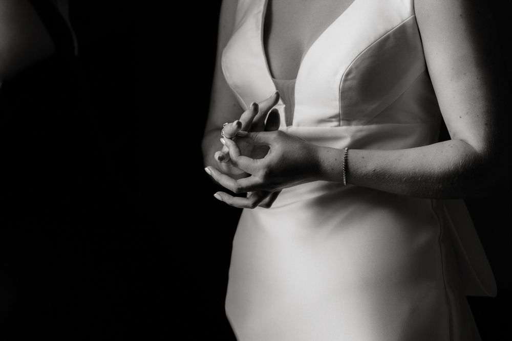 Close-up black and white photo of a bride in a white wedding dress clasping her hands together.