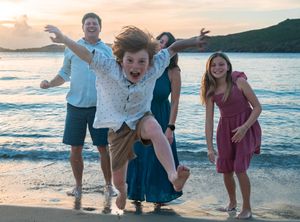 A boy jumps in front of his family on the beach.