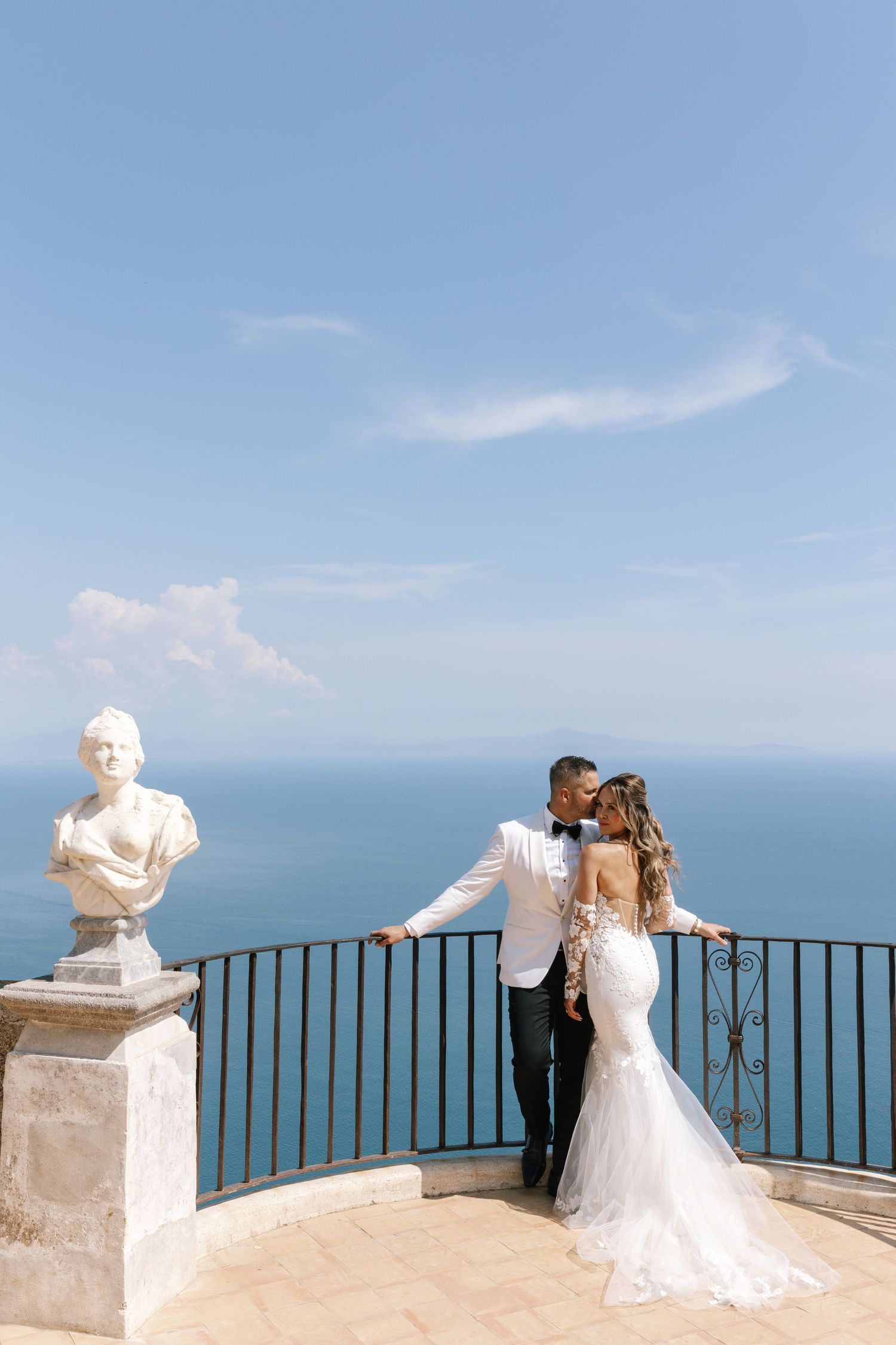 Bride in flowing white gown poses near fountain outside French chateau.