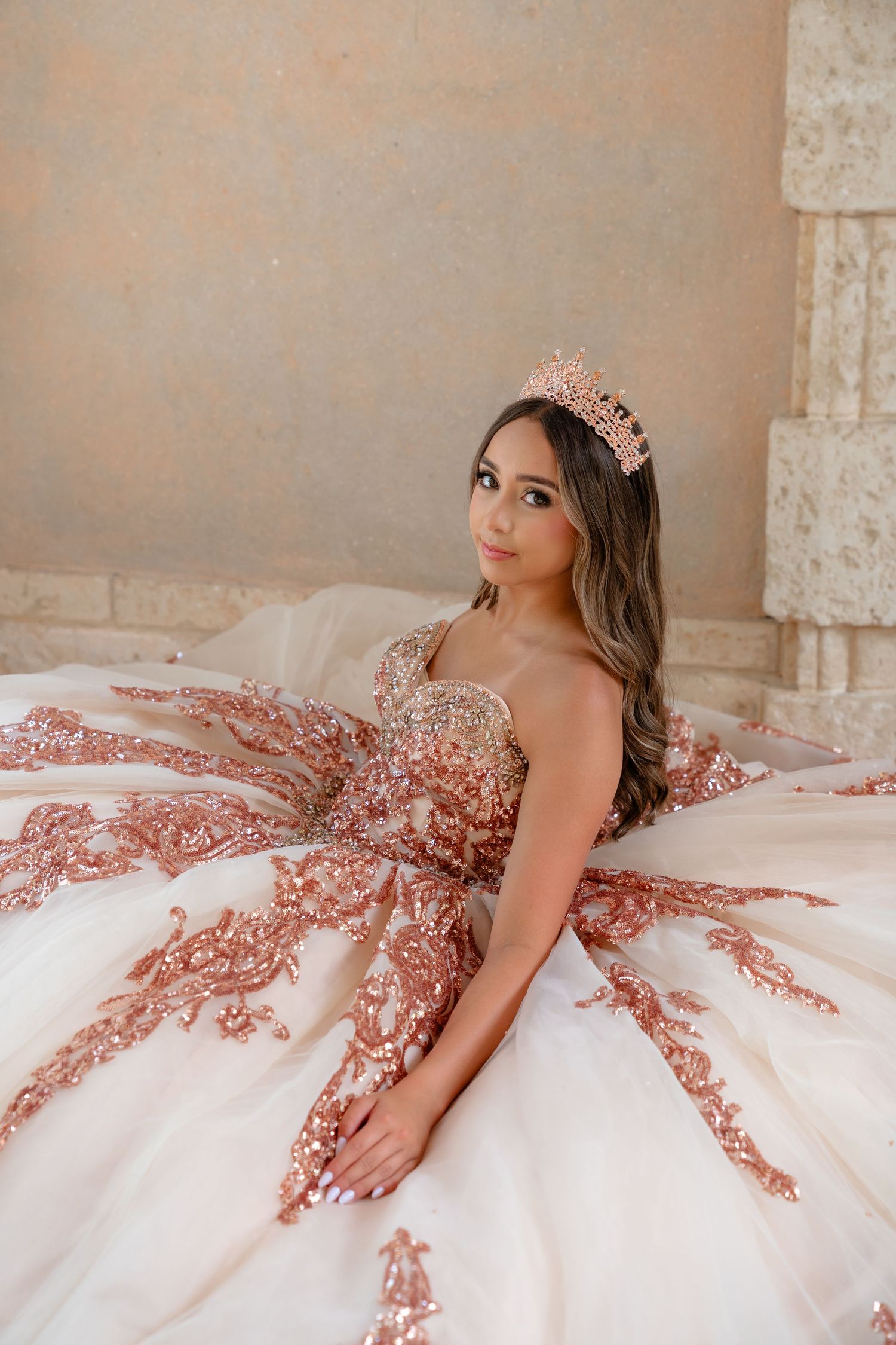 Beautiful young woman in a rose gold sequined quinceañera ball gown wearing a tiara crown.