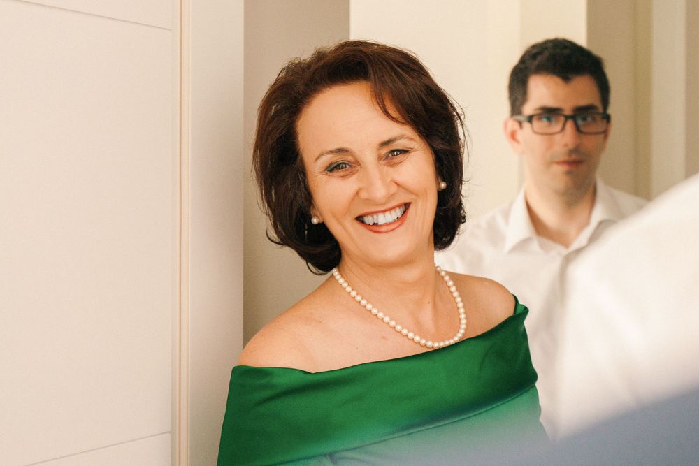 Smiling woman in green off-shoulder dress wearing pearl necklace at a formal event.