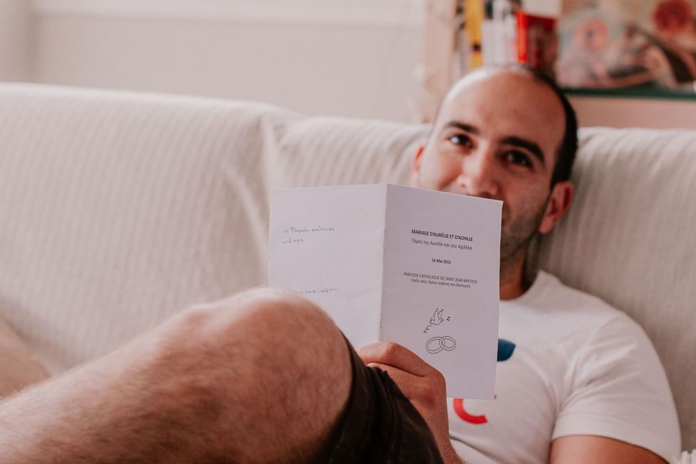 Man relaxing on white sofa holding and reading a small booklet or pamphlet indoors.