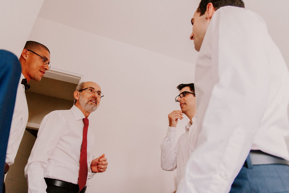 Group of men in white shirts and red tie having conversation during wedding preparations.